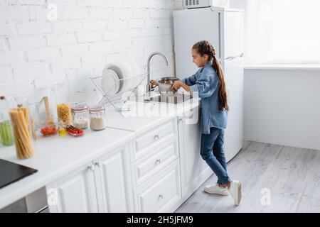 Seitenansicht des Kindes, das Wasser in den Topf in der Küche gießt Stockfoto