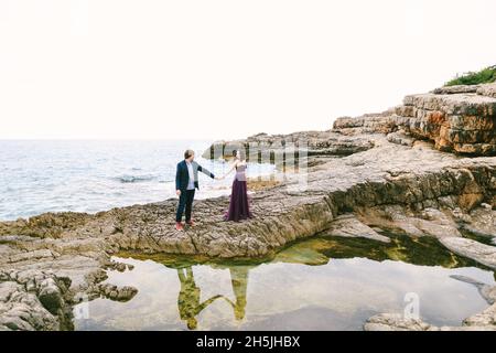 Mann und Frau stehen mit den Händen auf den Felsen vor dem Hintergrund des blauen Meeres und des Grüns Stockfoto