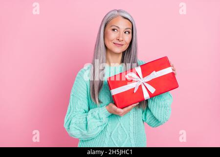 Foto von niedlichen grauen Frisur ältere Dame halten Geschenk aussehen leeren Raum tragen teal Pullover isoliert auf rosa Farbe Hintergrund Stockfoto