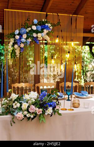 Hochzeits-Präsidium, Bankettsaal für Brautpaar mit Blumen, Grün, Blau- und Goldfarbe. Üppige Blumenarrangements auf dem Hochzeitstisch. Glühend Stockfoto