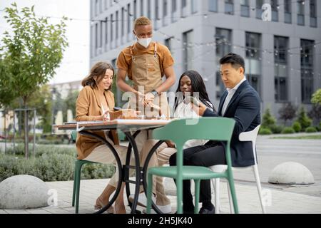 Der Kellner nimmt die Bestellung vom Gast im Cafe im Freien an Stockfoto