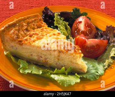 Portionsscheibe Quiche Lorraine gelb orange Platte garnieren von Salat in Scheiben geschnitten Tomaten rot strukturierten Hintergrund Stockfoto