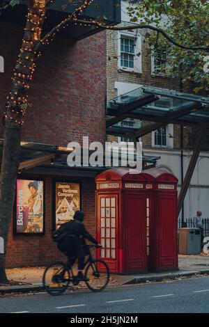 London, Großbritannien - 19. November 2020: Rote Telefonzellen vor dem Sadlers Wells Theater in London, Radfahrer fahren vorbei. Rote Telefonzellen finden Sie in curr Stockfoto