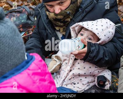 Narewka, Polen. November 2021. Eine Frau sah, wie sie ein sieben Monate altes Baby im eisigen Wald fütterte.Eine siebzehnköpfige Flüchtlingsfamilie, darunter neun Kinder aus Dohuk, Irak, verbrachte siebzehn Tage in einem Wald an der polnischen Grenze von Belarus und wurde achtmal zurückgedrängt. Verzweifelt mit einem sieben Monate alten Baby und einer älteren Frau mit Beinproblemen beschlossen sie, Aktivisten um Hilfe zu bitten. Kredit: SOPA Images Limited/Alamy Live Nachrichten Stockfoto