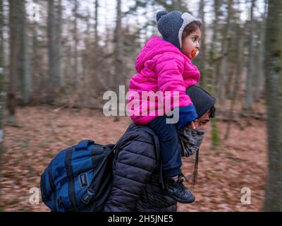 Narewka, Polen. November 2021. Der junge Mann trägt ein kleines Mädchen über seinen Schultern, während er im Wald nahe der Grenze zu Weißrussland spaziert. Eine siebzehnköpfige Flüchtlingsfamilie, darunter neun Kinder aus Dohuk, Irak, verbrachte siebzehn Tage in einem Wald an der polnischen Grenze von Belarus und wurde achtmal zurückgedrängt. Verzweifelt mit einem sieben Monate alten Baby und einer älteren Frau mit Beinproblemen beschlossen sie, Aktivisten um Hilfe zu bitten. Kredit: SOPA Images Limited/Alamy Live Nachrichten Stockfoto