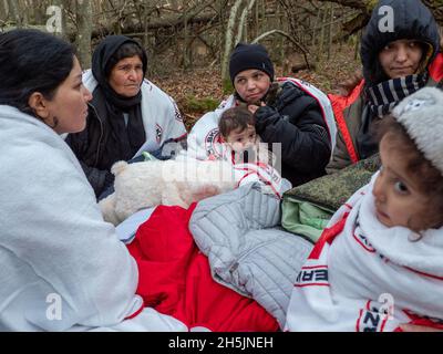 Narewka, Polen. November 2021. Die Familie sitzt in einem Wald und wärmt sich unter Decken, die von der Organisation Grupa Granica zur Verfügung gestellt werden.Eine siebzehnköpfige Flüchtlingsfamilie, darunter neun Kinder aus Dohuk, Irak, verbrachte siebzehn Tage in einem Wald an der polnischen Grenze von Belarus und wurde achtmal zurückgedrängt. Verzweifelt mit einem sieben Monate alten Baby und einer älteren Frau mit Beinproblemen beschlossen sie, Aktivisten um Hilfe zu bitten. Kredit: SOPA Images Limited/Alamy Live Nachrichten Stockfoto