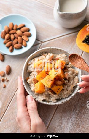 Haferflocken mit gehackter Papaya, Mandeln und Chiasamen in weiblichen Händen. Gesunde vegane Frühstückschale Draufsicht Stockfoto