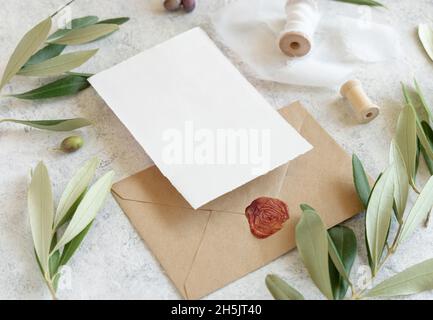 Hochzeitseinladungskarten und Umschläge auf einem weißen Marmortisch mit Olivenzweigen aus nächster Nähe. Elegante moderne Vorlage mit horizontalen leeren Papierkarten Stockfoto