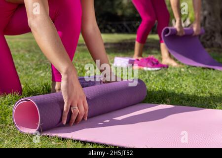 Zwei Frauen Rollen Pilates Matten in einem Park an einem sonnigen Tag im Sommer. Kaukasische Frauen in rosa Kleidung, die im Freien Sport treiben. Sport und gesundes Livestyl Stockfoto