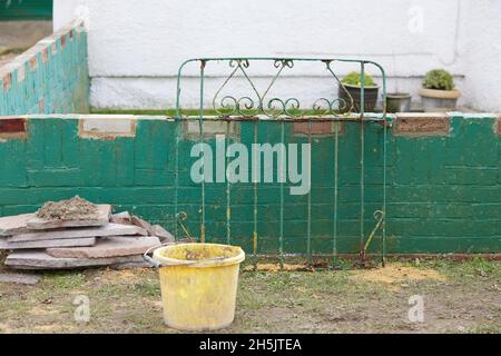 Stapel von Gebäudeplatten, die gegen eine vernachlässigte grüne Wand und ein Gartentor gesehen werden. Stockfoto