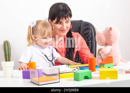 Der Kinderarzt legte ein Stethoskop auf das Mädchen einer 3-4-jährigen Patientin und spielt mit ihr in einem Spielzeug. Psychologischer Kontakt eines Arztes mit einem Kind, Stockfoto