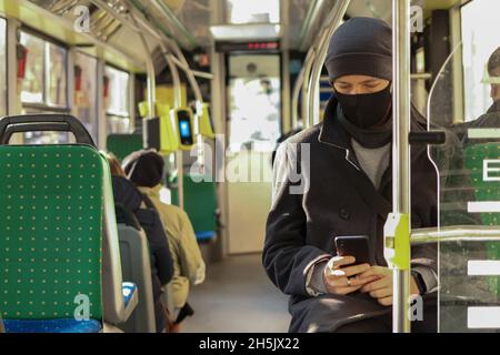 Junger Mann in einer Gesichtsmaske mit einem Smartphone für soziale Medien im öffentlichen Verkehr Stockfoto