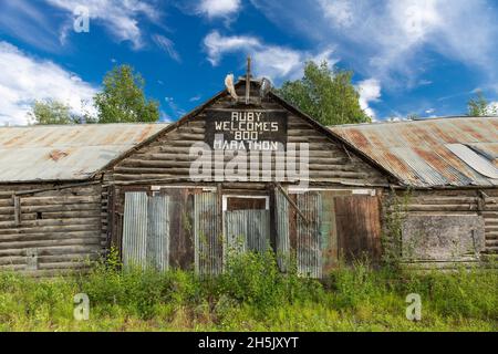 Ein Schild für den „Ruby Signes 800 Marathon“ ist im Sommer auf einer alten Blockhütte, Ruby, Interior Alaska, USA, ausgestellt Stockfoto