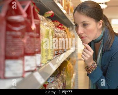 Frau, die sich Nährwertkennzeichnungen auf Verpackungen im Regal im Supermarkt ansieht; Deutschland Stockfoto