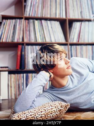 Teenager-Junge lag auf dem Boden vor der Plattenalbum-Sammlung und blickte mit einem nachdenklichen Ausdruck nach oben; Deutschland Stockfoto