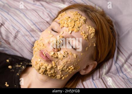 Eine Frau macht zu Hause eine kosmetische Maske aus Haferflocken auf ihr Gesicht. Anti-Aging-Behandlungen, Hautpflegekonzept. Stockfoto