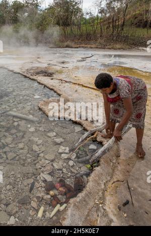 Frau, die in den Dei Dei Thermal Hot Springs auf Fergusson Island, D'Entrecasteaux Islands, Papua-Neuguinea, Yams kocht Stockfoto