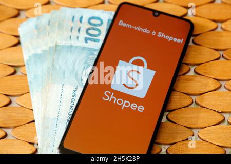 Minas Gerais, Brasilien - 19. April 2021: Smartphone-Handy-Bildschirm mit Shopee Marke und mehrere brasilianische echte Rechnungen Stockfoto