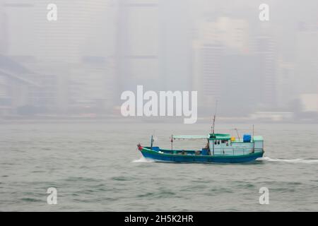 Ein Boot überquert den Hafen vor einer nebligen Hong Kong. Stockfoto