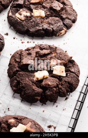 Eine vertikale Nahaufnahme mehrerer dunkler Schokoladenkekse auf Backpapier Stockfoto