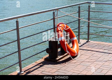 Eine Rettungsboje hängt am Geländer und wirft einen Schatten auf den Steinpier. Das Konzept der Sicherheit und des Dispatching Stockfoto