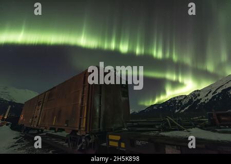 Aurora Borelais zeigen den Twentymile River mit Eisenbahnwaggons und Bergen in Girdwood; Alaska, Vereinigte Staaten von Amerika Stockfoto