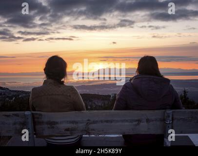 Blick von hinten auf zwei Freunde, die auf einer Bank sitzen und den wunderschönen Sonnenuntergang am Glen Alps Trailhead genießen Stockfoto