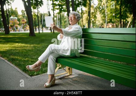 Eine ältere Frau in einer Brille mit einem Laptop auf der Bank Stockfoto