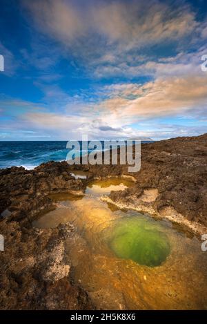 Vulkanische Felsformationen und Sonnenlicht, die sich im grünen Gezeitenpool am Strand von Pointe des Chateaux spiegeln Stockfoto