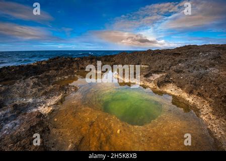 Vulkanische Felsformationen und Sonnenlicht, die sich im grünen Gezeitenpool am Strand von Pointe des Chateaux spiegeln Stockfoto