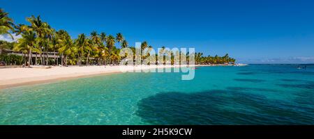 Die Menschen genießen das türkisfarbene Wasser des Karibischen Meeres mit Palmen am Sandstrand von Caravelle Beach, Sainte-Anne, Grande-Terre Stockfoto