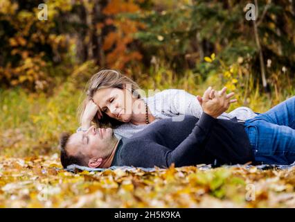 Ein reifes Ehepaar, das während der Herbstsaison gemeinsam in einem Stadtpark auf einer Decke auf den heruntergefallenen Blättern liegt Stockfoto
