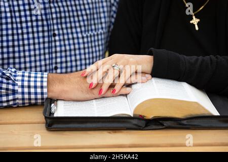 Ein reifes Paar, das sich an einem warmen Herbsttag in einem Stadtpark Zeit mit Hingabe teilt und die bibel an einem Picknicktisch studiert Stockfoto