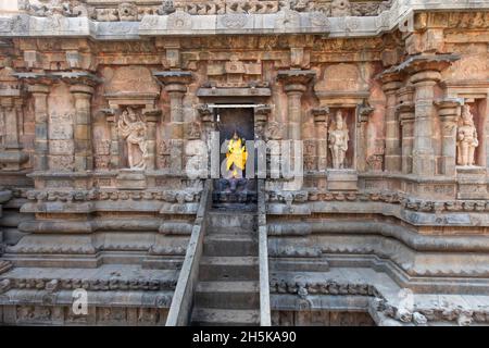 Eine Treppe führt zu einer Nische mit einer hinduistischen Gottheitsstatue, die in hellgelbe Seide gehüllt ist und in eine Steinwand des Dravidischen Chola-Tempels der Airavatesvara-Ära führt Stockfoto