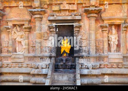 Nische mit hinduistischer Gottheitsstatue, eingewickelt in hellgelbe Seide in Steinwand des Dravidischen Chola-Tempels der Airavatesvara-Ära; Darasuram, Tamil Nadu, Indien Stockfoto