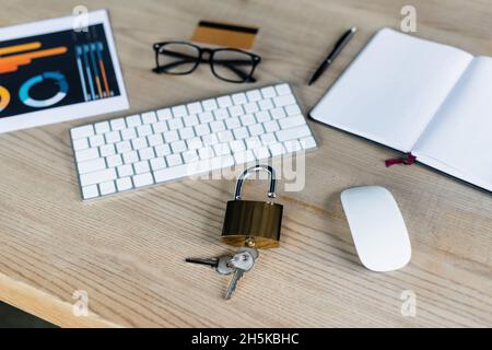 Vorhängeschloss mit Tasten in der Nähe von Computermaus, Tastatur und Notebook auf dem Tisch Stockfoto