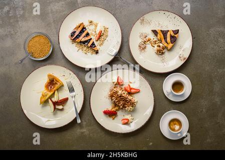 Blick von direkt oben auf eine Vielzahl von Kuchen auf Tellern mit Gabeln und Cappuccinos; Studio Stockfoto