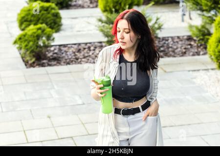 Die elegante Frau trägt ihre eigene wiederverwendbare Wasserflasche, die im Freien steht. Bleiben Sie hydratisiert, umweltfreundlich, keine Verschwendung und Green Living Lifestyle-Konzept. Stockfoto