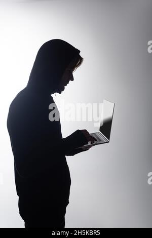 Seitenansicht des Hackers in der Haube mit Laptop isoliert auf grau Stockfoto