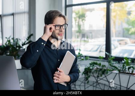 Programmierer hält Brillen und Papiermappe in der Nähe des Computers im Büro Stockfoto