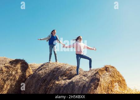 Zwei junge Schwestern, die auf einem Haufen Heuballen spielen; Alcomdale, Alberta, Kanada Stockfoto