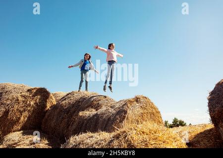 Zwei junge Schwestern, die auf einem Haufen Heuballen spielen; Alcomdale, Alberta, Kanada Stockfoto