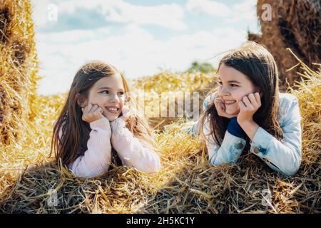 Zwei junge Schwestern, die auf ihrer Familienfarm auf Heuballen liegen, verbringen eine gute Zeit miteinander; Alcomdale, Alberta, Kanada Stockfoto