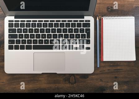 Draufsicht auf Laptop-Computer und leeres Notizblock mit Bleistift auf Holzschreibtisch Stockfoto