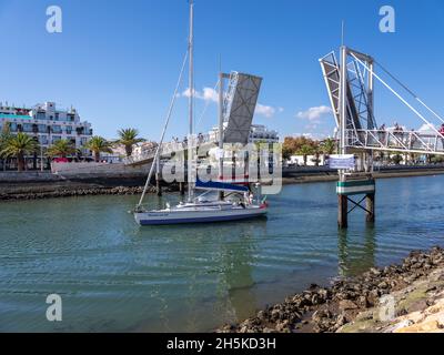 Lagos, Algarve, Portugal - 10 2021. November: Yacht, die vom Yachthafen entlang des Flusses Bensafrim durch die offene Bascule-Fußgängerbrücke fährt. Stockfoto