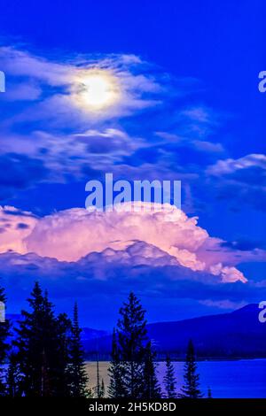 Vollmond in einem blauen Himmel, der die rosa Gewitterwolken über dem mondbeleuchteten Wasser im Thorofare im Upper Yellowstone River Valley, Yellowstone ... Stockfoto