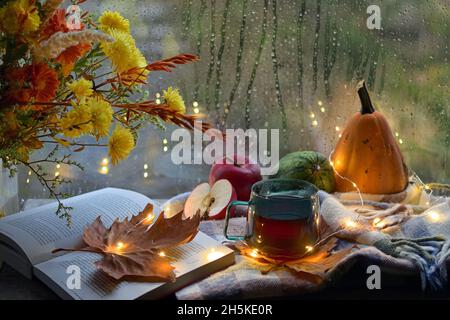 Herbstdekor mit Blumen, offenem Buch und einer Tasse Tee Stockfoto