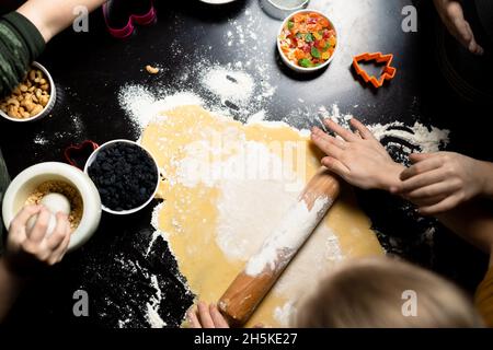 Kinder Rollen den Teig aus, um Geburtstagskekse zu machen. Küchenzubereitungen. Gemeinsame Aktivitäten in der Familie. Stockfoto