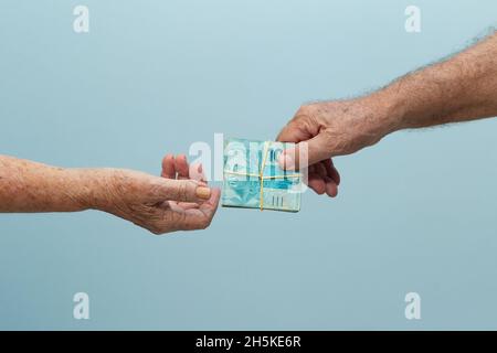 Hand eines älteren Mannes, der an eine andere Person bezahlt. Hände von zwei älteren Menschen, die sich gegenseitig Geld geben. Bezahlen und Empfangen von Geld. Stockfoto