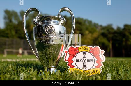 30. August 2021, Leverkusen, Deutschland. Bayer 04 Leverkusen Fußballverein-Emblem und UEFA Champions League Cup auf einem grünen Rasen. Stockfoto